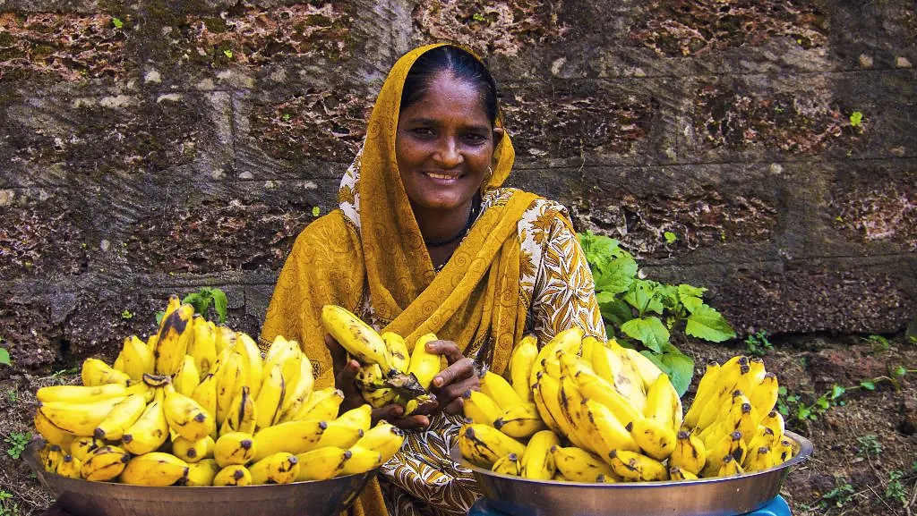 A smiling woman vendor selling bananas from large metal bowls