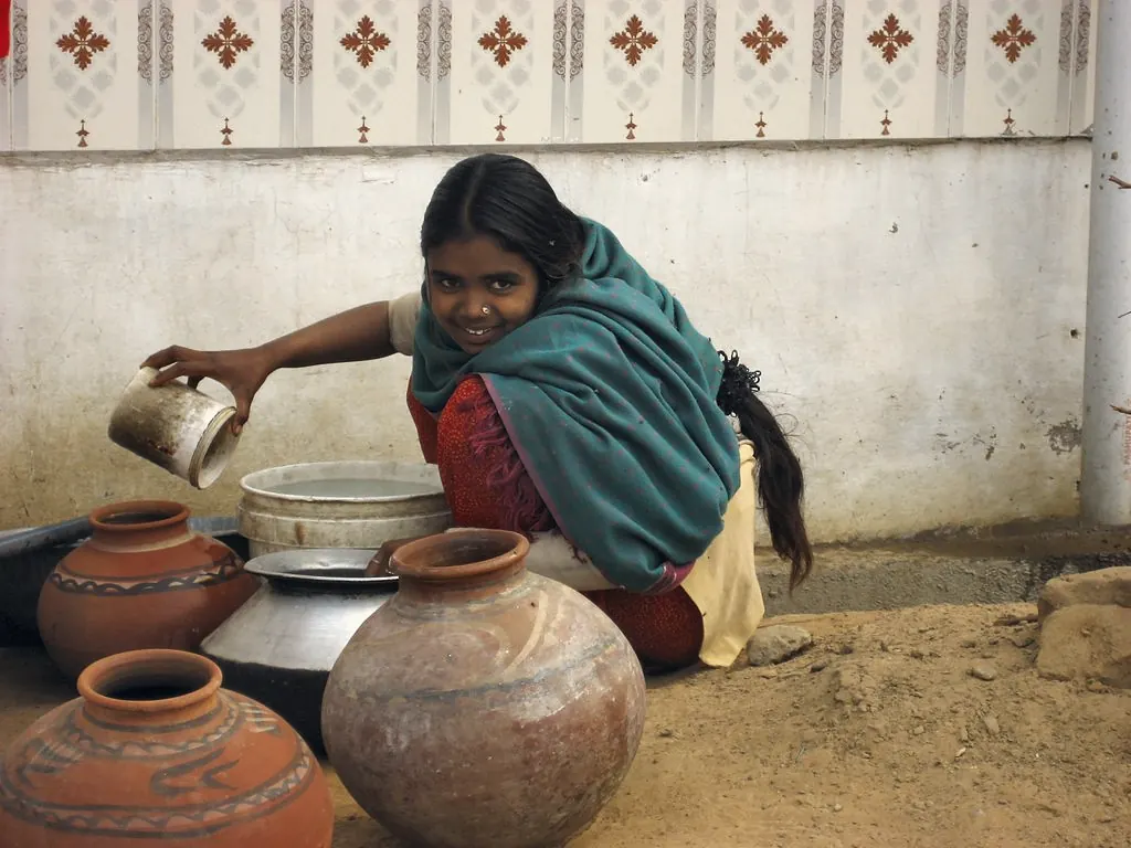 A girl pouring water into clay pots outside her home