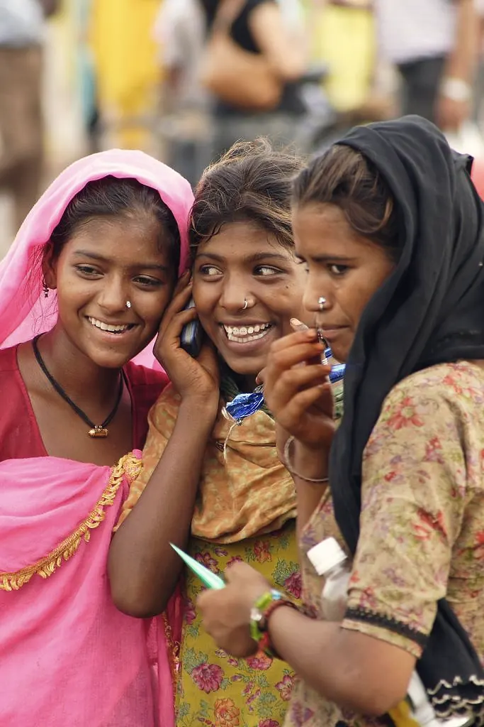 Three young women laughing together while using a mobile phone