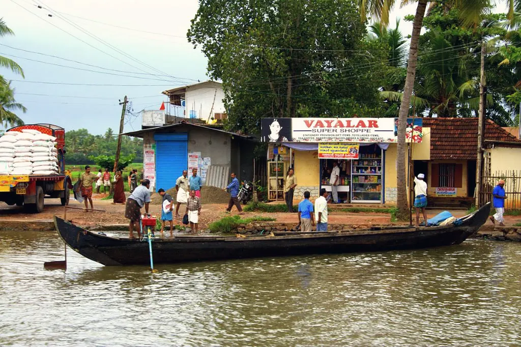 A rural Kerala riverside with a village shop and a passenger canoe