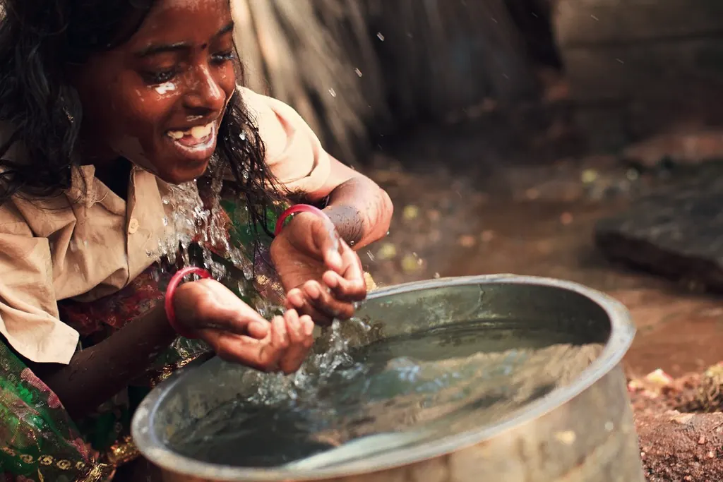A young woman splashing clean water on her face from a metal pot