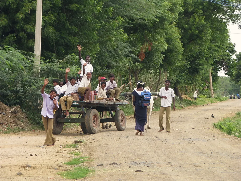 Children waving from a bullock cart on a rural road on their way to school