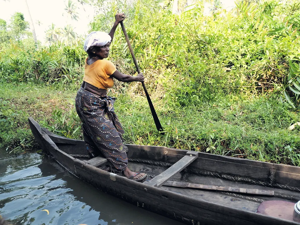 A woman poling a wooden canoe through green waterways in Kerala