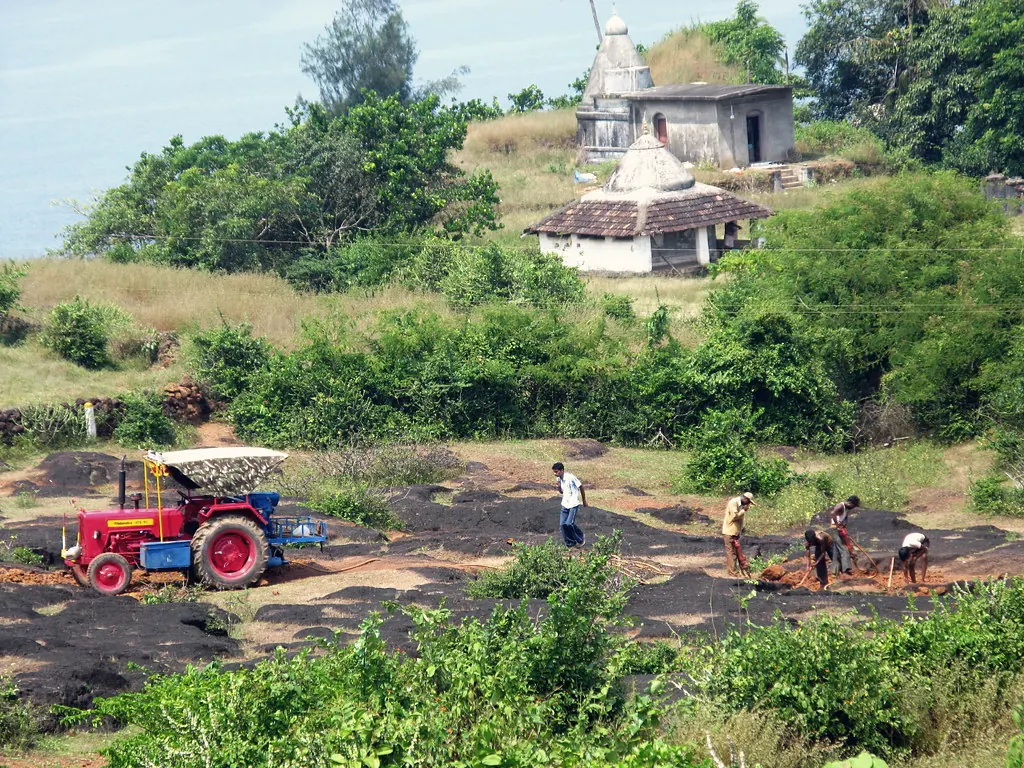 A tractor and farm workers preparing land on a hillside in Karnataka